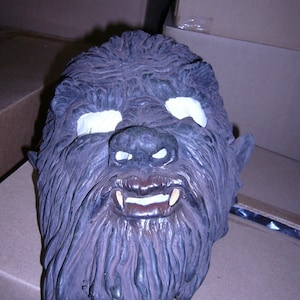 May include: A werewolf mask with a furry face, white eyes, and sharp teeth. The mask is made of a dark gray material and has a realistic look.