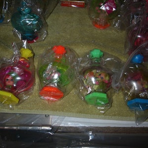 May include: Five clear plastic bubble toys with colorful bases and small dolls inside. The dolls have long hair and are wearing colorful dresses. The toys are packaged in clear plastic bags.