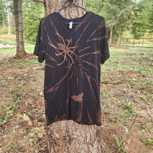 May include: Black t-shirt with a tie-dye pattern and brown printed images of a spider and a butterfly.