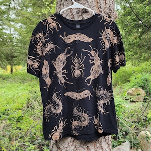 May include: Black t-shirt featuring a brown print of various insects, including ants, slugs, and centipedes.