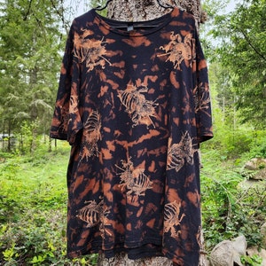 Puede incluir: Camiseta negra con un patrón de tie-dye y siluetas de insectos marrones.