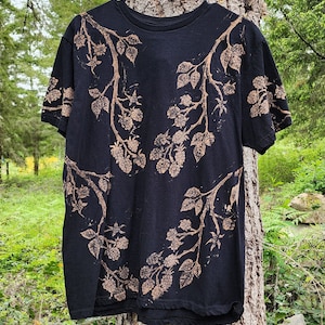 Puede incluir: Camiseta negra con un diseño de ramas y bayas de mora teñidas con lejía.