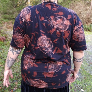 Pode incluir: Camiseta preta com um padrão tie-dye marrom e branco com uma imagem repetida de um fóssil de trilobite.