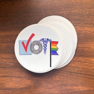 May include: A white sticker with the word "VOTE" in blue and red. The "O" is replaced with a stylized medical symbol, and the "T" is replaced with a rainbow flag.