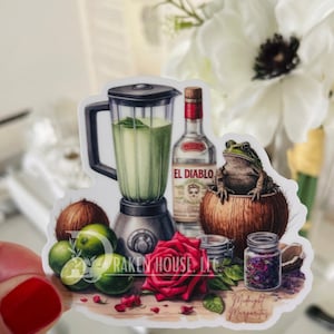 May include: A sticker featuring a blender with a green drink, a bottle of tequila labeled "El Diablo", a coconut with a frog sitting on top, a red rose, limes, and two jars with purple flowers. The text "Midnight Margaritas" is at the bottom of the sticker.