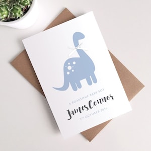 Tarjeta personalizada para recién nacido: adorable tarjeta de felicitación con lazo azul y dinosaurio rugiente.