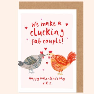 Puede incluir: Tarjeta de San Valentín con una ilustración en acuarela de dos pollos enfrentados. La tarjeta dice "We make a clucking fab couple!" en rojo, con "Happy Valentine's Day" debajo. Pequeños corazones están esparcidos alrededor del texto.