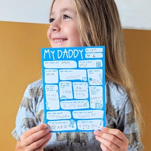 Op de afbeelding: Een felblauwe rechthoekige kaart met de titel My Daddy, witte gedrukte tekst en handgeschreven antwoorden in blauwe inkt. De kaart bevat diverse vragen over een vaderfiguur, waaronder leeftijd, lengte, lievelingseten, beroep en een persoonlijke boodschap.