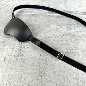 May include: A black eye patch with an adjustable strap. The strap is made of elastic material and has a metal buckle.