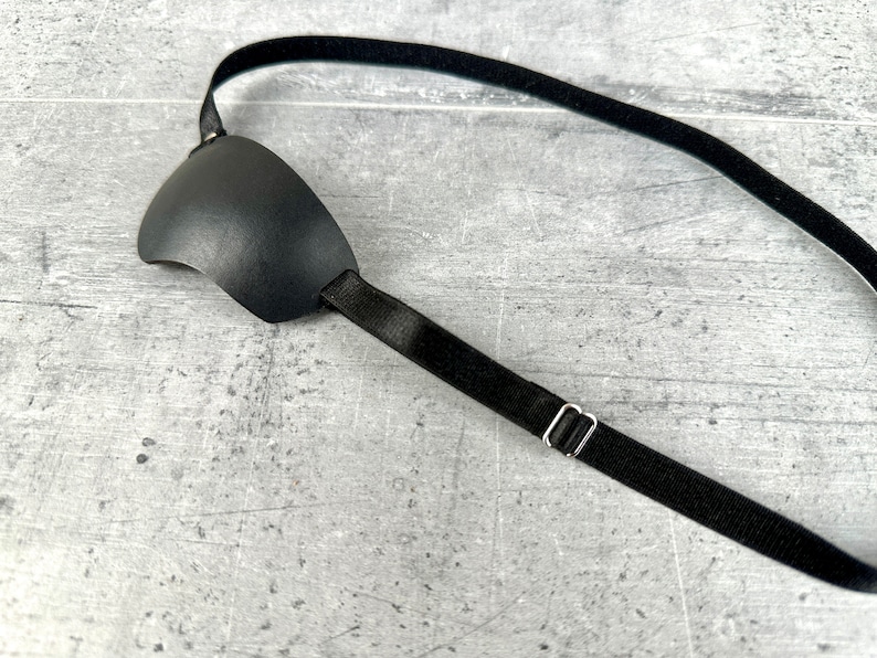 May include: A black eye patch with an adjustable strap. The strap is made of elastic material and has a metal buckle.