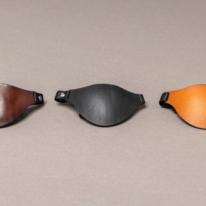 May include: Three leather eye patches in brown, black, and orange. Each patch has a black strap with a silver rivet.