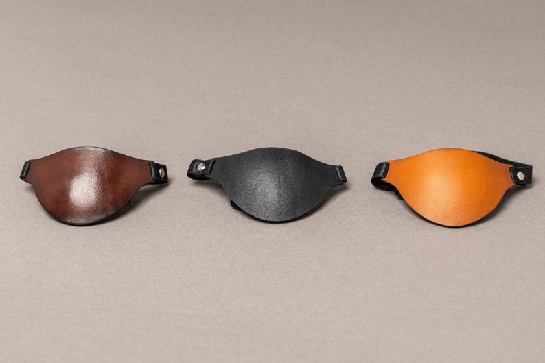 May include: Three leather eye patches in brown, black, and orange. Each patch has a black strap with a silver rivet.