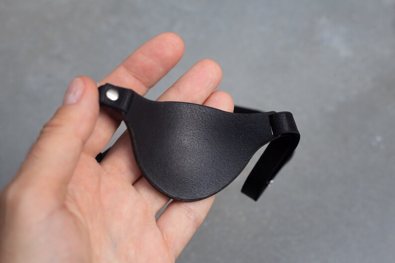 May include: A black leather eye patch with an adjustable strap. The patch has a smooth, textured surface.
