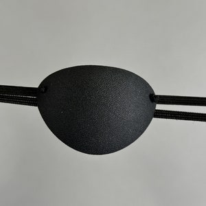 May include: A black eye patch with an elastic strap. The patch is made of a soft, textured material.