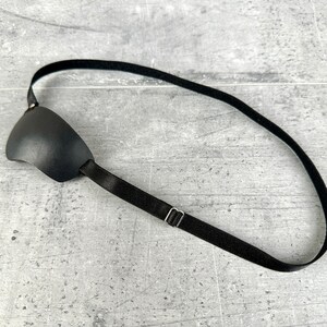 May include: A black eye patch with an adjustable strap. The strap has a metal slider for adjusting the fit.