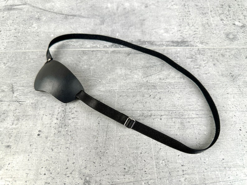 May include: A black eye patch with an adjustable strap. The strap has a metal slider for adjusting the fit.