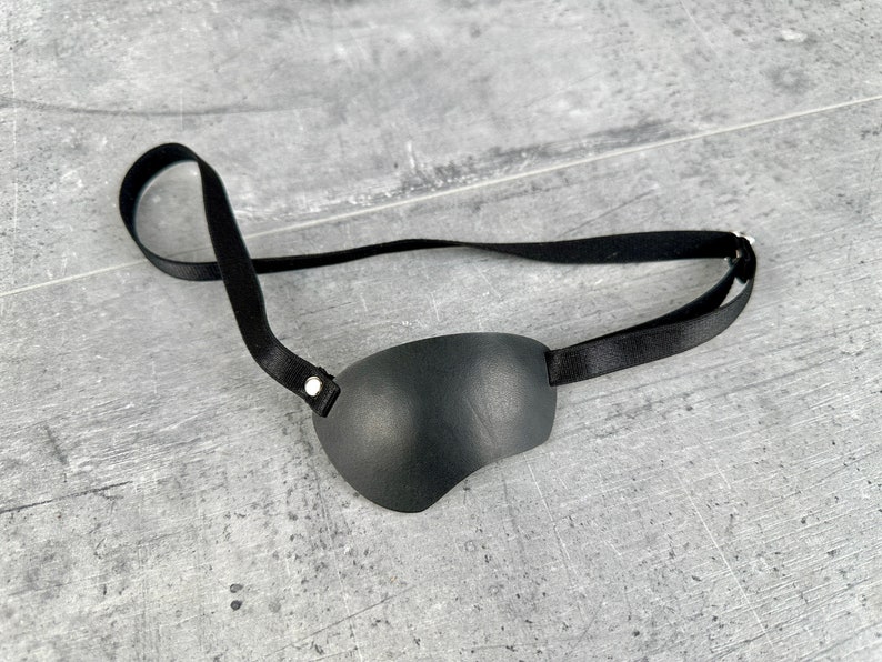 May include: A black leather eye patch with an adjustable strap. The patch is designed to cover one eye.