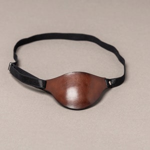 May include: A brown leather eye patch with a black elastic strap.