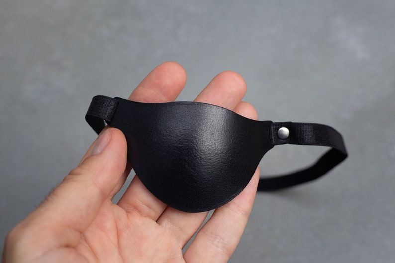 May include: A black leather eye patch with an adjustable elastic strap and a silver metal buckle.