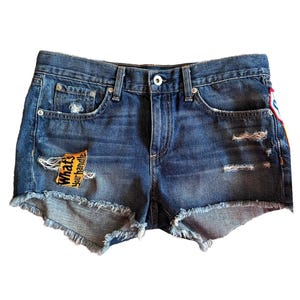 May include: Blue denim shorts with distressed details, featuring a frayed hem and a patch that reads "What's Your Handle". The shorts have a classic five-pocket design and a button closure.