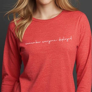 May include: A red long-sleeve shirt with the text "remember everyone deployed" in white script. The shirt is made of a soft material and has a crew neck.
