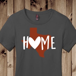May include: A dark gray t-shirt with a red outline of the state of Texas and the word "HOME" with a white heart in the middle of the state.