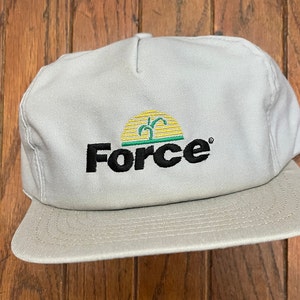 Könnte beinhalten: Eine hellbeige Baseballkappe mit strukturierter Krone und flachem Schirm. Auf der Vorderseite befindet sich ein gesticktes Logo mit dem Wort Force in schwarzen Buchstaben unter einer gelben Sonnengrafik mit einem grünen Pflanzenspross.