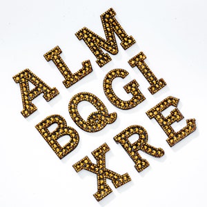 Pu&ograve; includere: Lettere dorate dell'alfabeto, A, L, M, B, Q, G, I, X, R ed E, realizzate con strass.