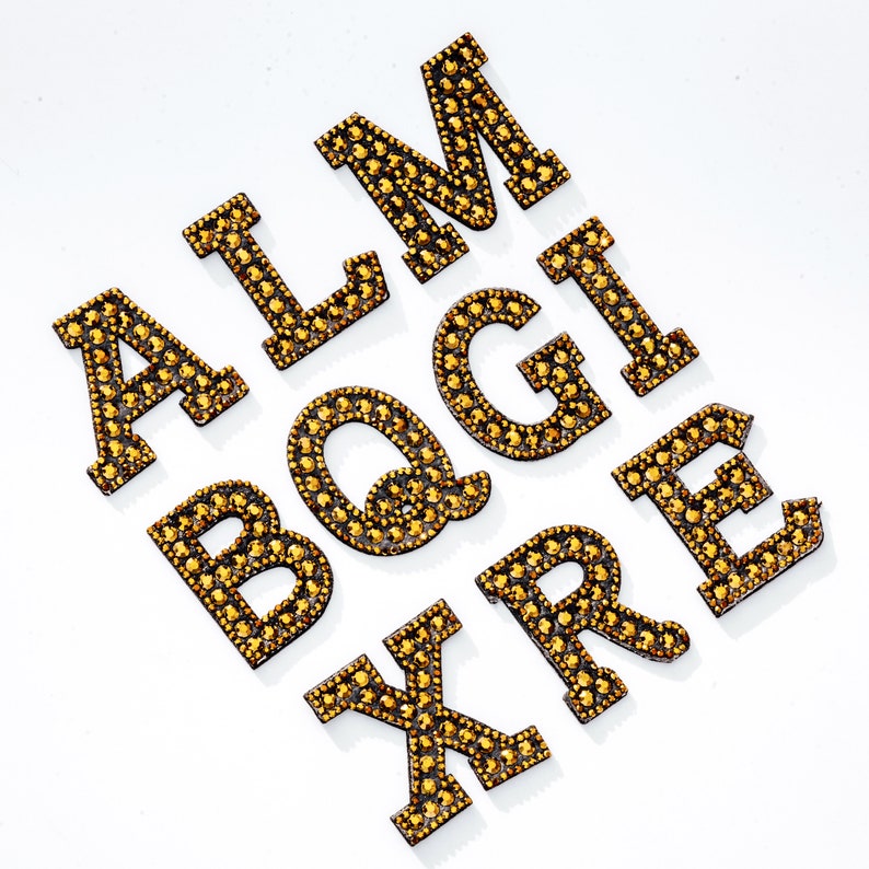 Pu&ograve; includere: Lettere dorate dell'alfabeto, A, L, M, B, Q, G, I, X, R ed E, realizzate con strass.