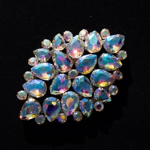 May include: A cluster of iridescent teardrop-shaped rhinestones arranged in a leaf-like pattern on a black background.