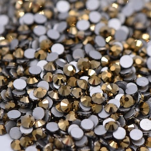 May include: A pile of gold-colored rhinestones with silver adhesive backs. The rhinestones are small and round, and they are arranged in a random pattern.
