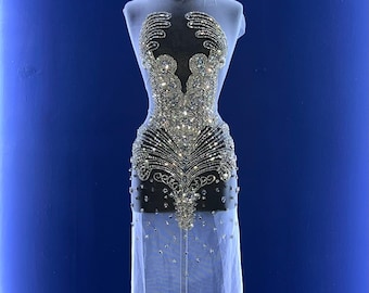 Könnte beinhalten: Ein weißes, durchsichtiges Kleid mit einem Kristallbesatz. Das Design zeigt ein großes, kompliziertes Muster aus Kristallen in Silber.