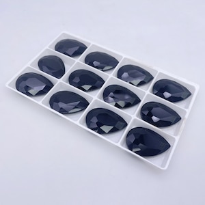 May include: A white tray with 12 black teardrop-shaped glass rhinestones.