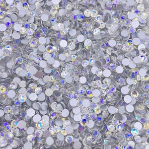 May include: A close-up image of a large quantity of clear glass rhinestones with a silver backing. The rhinestones are scattered randomly and appear to be of various sizes.