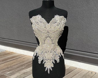 Peut inclure: Un corsage blanc perlé et pailleté avec un décolleté en cœur. Le corsage est sur un mannequin noir.