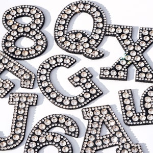May include: A set of letters and numbers covered in rhinestones. The letters are Q, X, J, G, and A. The numbers are 8 and 6.