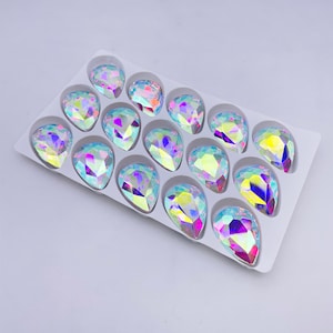 May include: A package of 15 iridescent teardrop-shaped rhinestones in a white plastic tray.