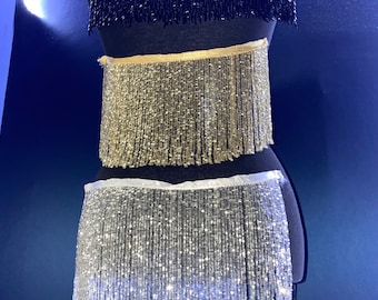 May include: Three different trims of beaded fringe, black, gold, and silver, displayed on a mannequin.