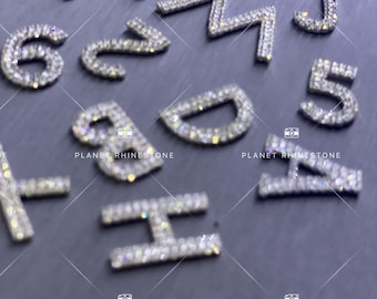 Può includere: Un set di lettere e numeri in strass argentati, tra cui le lettere I, M, W, J e D, e i numeri 5, 6 e 2. Le lettere e i numeri sono tutti realizzati con piccoli strass trasparenti.