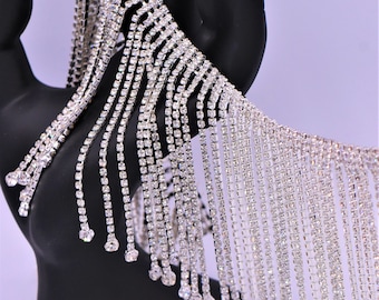 May include: Silver rhinestone fringe trim with a chain-like design. The fringe is made of small, clear rhinestones that are sewn onto a silver chain. The fringe is approximately 1 inch wide and is perfect for adding a touch of sparkle to any project.