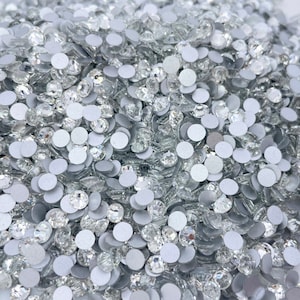 May include: A large pile of clear glass rhinestones with silver backs. The rhinestones are scattered randomly and are all the same size.
