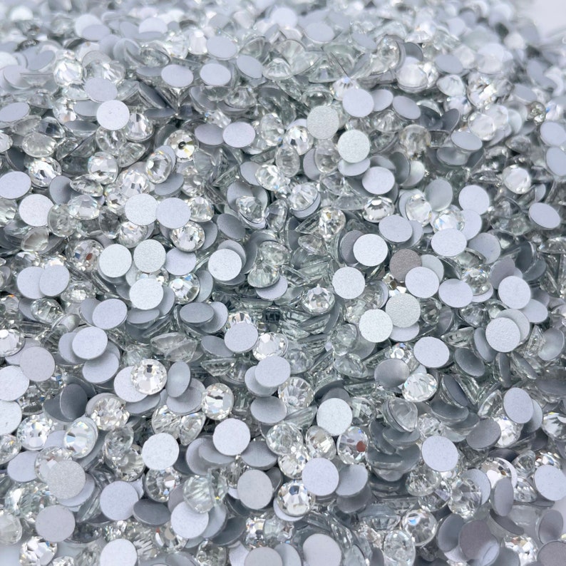 May include: A large pile of clear glass rhinestones with silver backs. The rhinestones are scattered randomly and are all the same size.