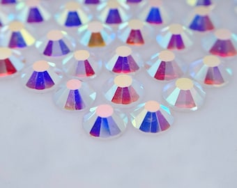 May include: A close-up of iridescent clear rhinestones arranged in a staggered pattern. The rhinestones have a rainbow effect and are arranged in a semi-circle.