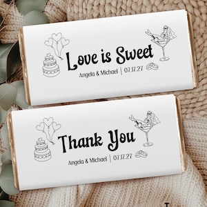 May include: Two white chocolate bar wrappers with black text and illustrations. One says "Love is Sweet" and the other says "Thank You". Both include names and a date. The wrappers have a wedding theme.