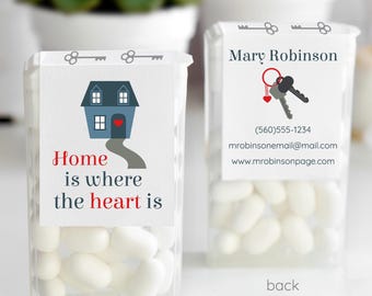 May include: Two clear plastic containers filled with white candies. One has a label with a blue house graphic and the text "Home is where the heart is." The other has a label with keys and contact information. Succulents are in the background.