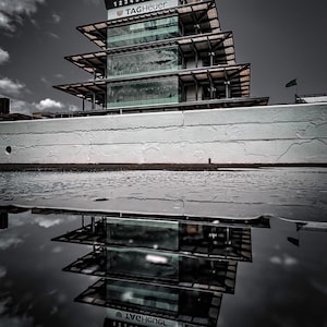 May include: A multi-tiered structure with glass and metal construction, featuring the TAG Heuer logo and numbers 1-10. The building's reflection is visible in the water below, creating a symmetrical image. The sky is overcast.