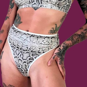 Könnte beinhalten: Hoher Höschen mit weißem Saum und Schlangenhaut-Muster. Die Unterwäsche ist aus weichem, dehnbarem Stoff und hat einen hohen Beinausschnitt.