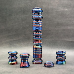 May include: A set of decorative metal objects with a striped pattern in blue, red, and gold. The collection includes a tall, cylindrical piece and several smaller components. The objects have a metallic sheen and are likely made of metal.