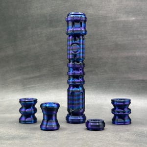 May include: A collection of blue and purple metal objects. The set includes a tall, cylindrical piece with a detailed design, along with several smaller, decorative components. The items have a metallic sheen and a textured appearance.
