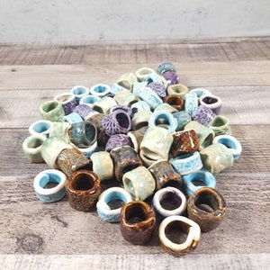 Pu&ograve; includere: Un mucchio di anelli in ceramica di vari colori, tra cui blu, verde, marrone e viola. Gli anelli sono di diverse dimensioni e forme e sono disposti in un motivo casuale.